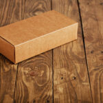 Craft unlabeled cardboard package box presented on stressed brushed wooden table, closeup