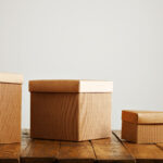 Different sized and shaped beige paper boxes on a wooden table in a studio with white walls